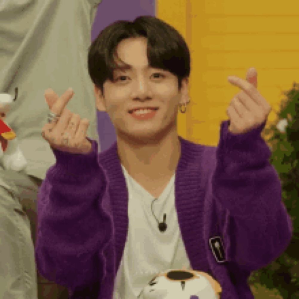 a young man wearing a purple cardigan and a white shirt is making a heart shape with his hands .