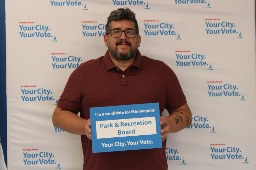 Jason Garcia holding a sign that says “I’m a candidate for Minneapolis Park & Recreation Board. Your city. Your vote.”