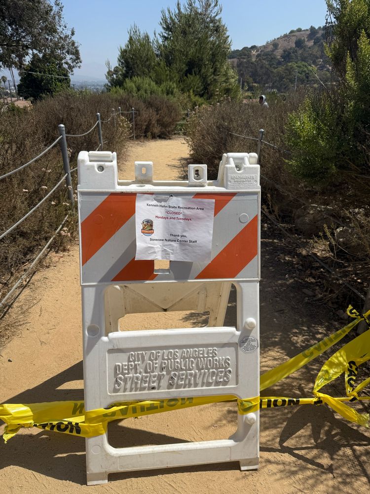 Caution tape and a closed sign blocking the park trail