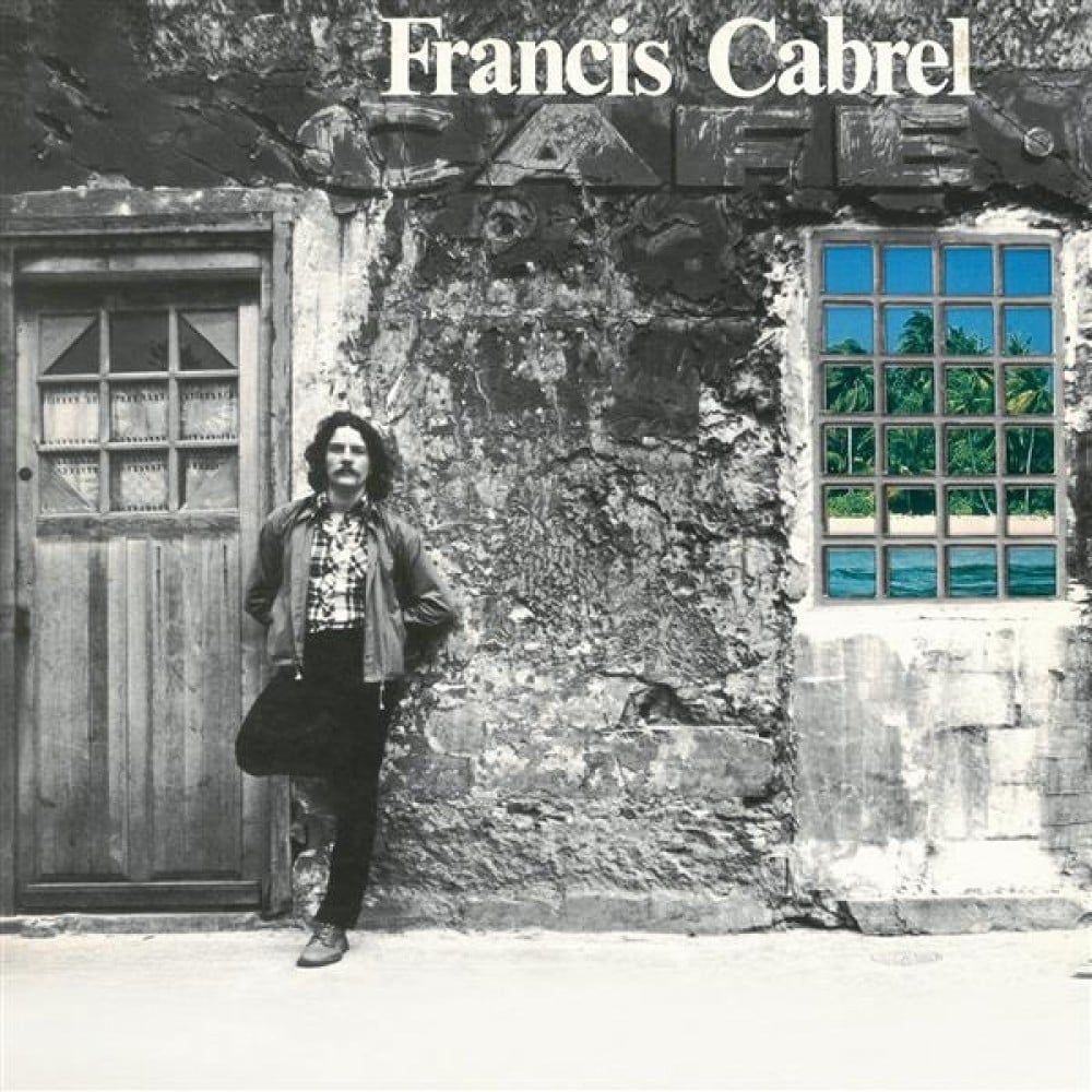 Cover of the Francis Cabrel album Les Murs de poussière.  A man with long hair and a moustache is leaning up against a wall.  To his left is an old door.  The photo is in black and white except for the window to his right, which shows a seaside scene with blue sky, water, sand, and palm trees.