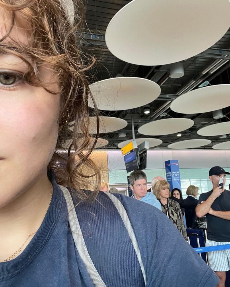 An ‘over-shoulder’ photo taken in the boarding queue. Behind Phoenix’s shoulder is a man in a blue top: Noel Gallagher. 