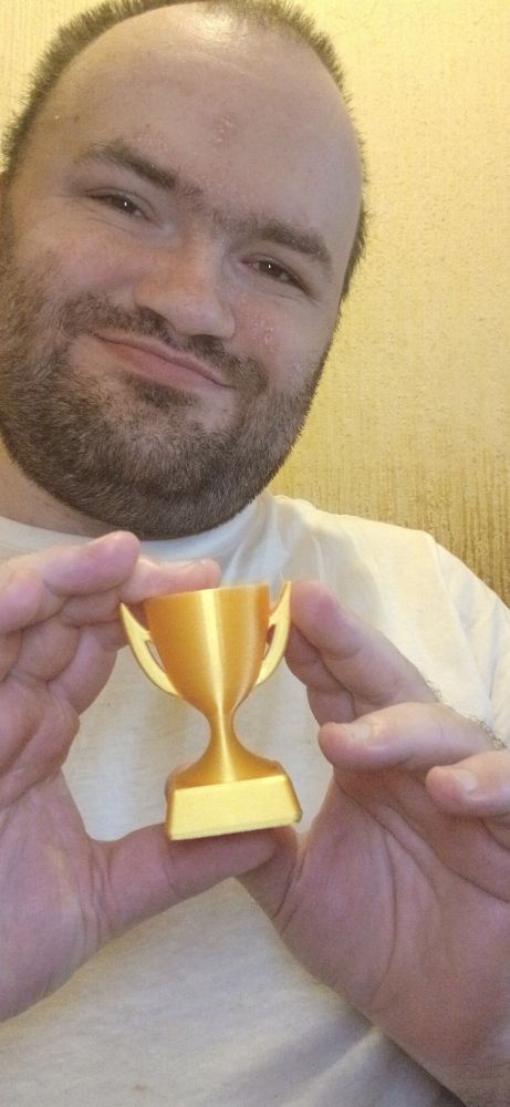 Me against a beige wall wearing a white tee shirt holding a gold trophy. 