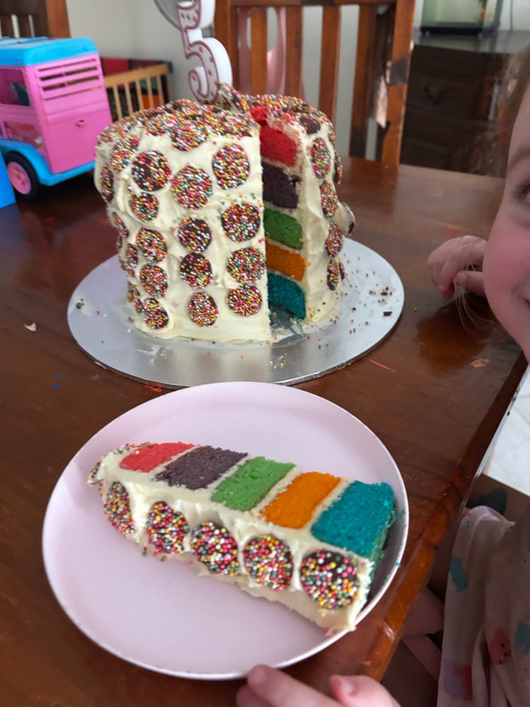 Sliced open cake. Rainbow coloured, layered cake with white icing and freckles 