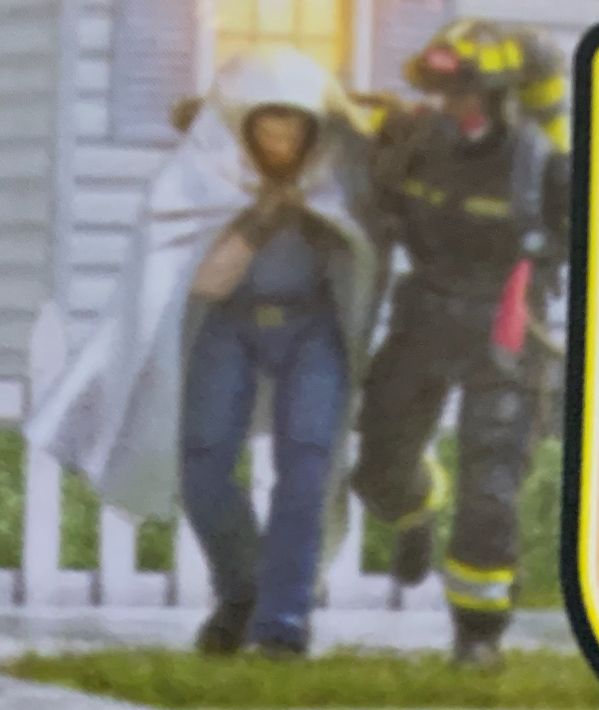 A firefighter escorting a man wrapped in a fire blanket away from a burning house. The man bears a strong resemblance to the GI Joe Classified Shipwreck figyre.