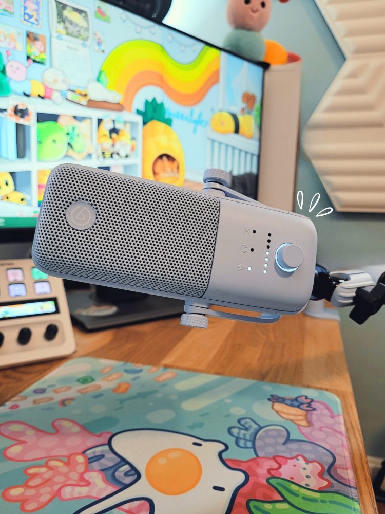 the light blue wave:3 microphone in my setup where you can see my blue sea themed desk mat, my elgato stream deck in white, my stream background, my blue painted walls, elgato audio panels and a catepillar plushie. there's an added little white accent next to the microphone to highlight it.