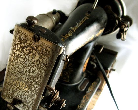 Photo of a vintage Singer sewing machine. The face plate facing front is ornately decorated and the machine is black.