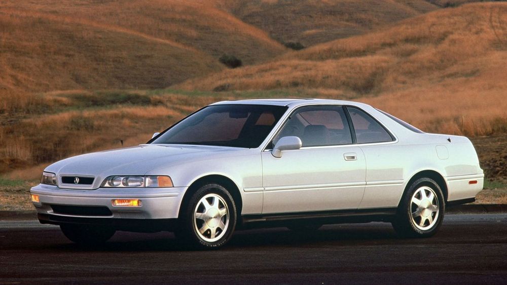 a promotional shot of a white 2nd generation (1991-1995) Acura Legend coupe against rolling hills covered in brownish grass