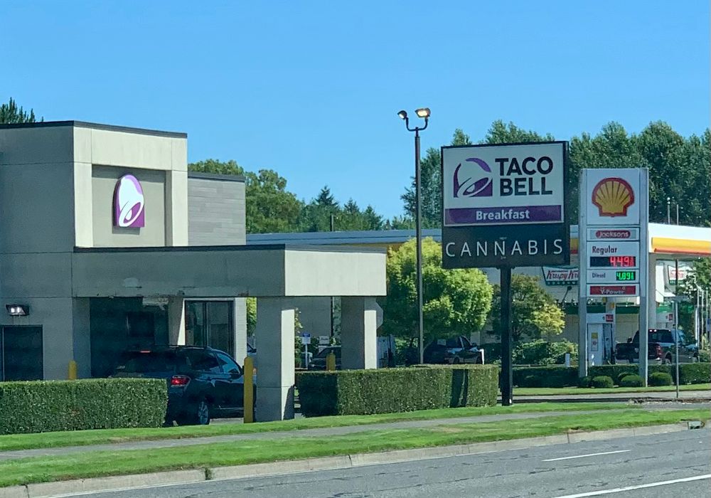 Picture of a Taco Bell drive through. Sign next to building reads:
TACO
BELL
Breakfast
CANNABIS 