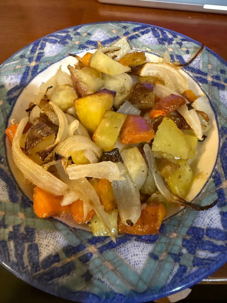 A ceramic bowl filled with roast onions, potatoes, and carrots. 