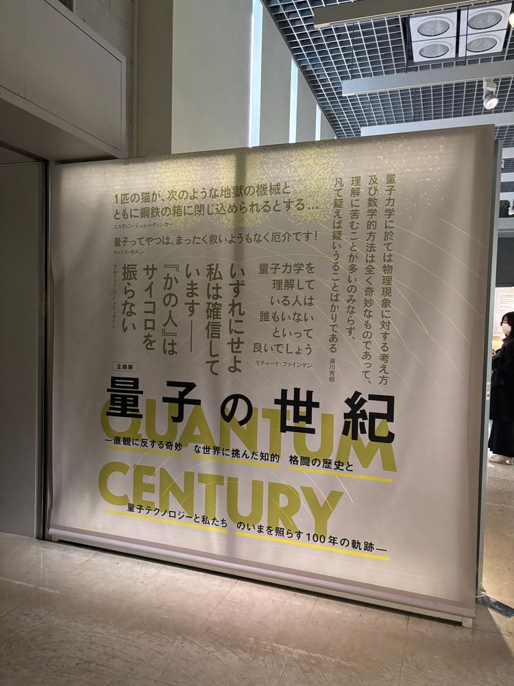 Entrance to the exhibition “quantum century” with black and green text on a white banner. 