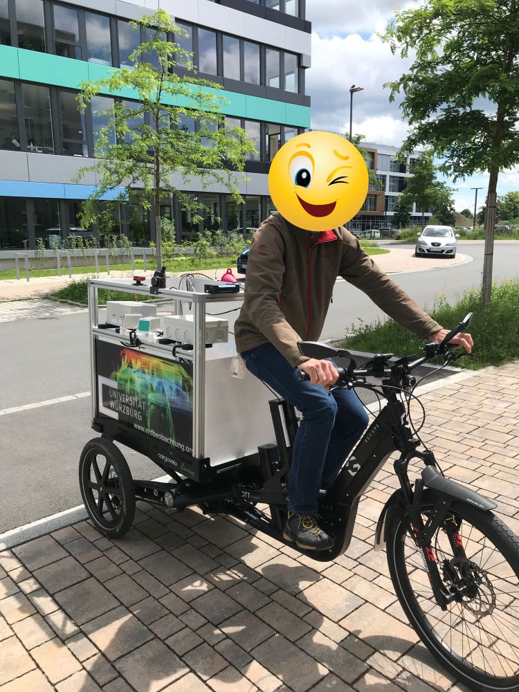 Lastenrad in einer Einfahrt, rechteckiges Gestell auf der Ladeplatatform mit allerlei Messgerät und Schild: "Universität Würzburg"

Der Fahrer wurde durch einen Zwinker-Smiley unkenntlich gemacht.