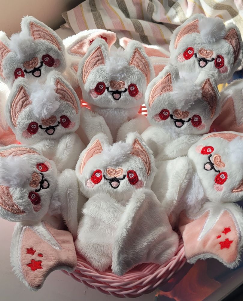 A pink basket full of small, plush, albino bats. They have red eyes and red stars on their wings. 