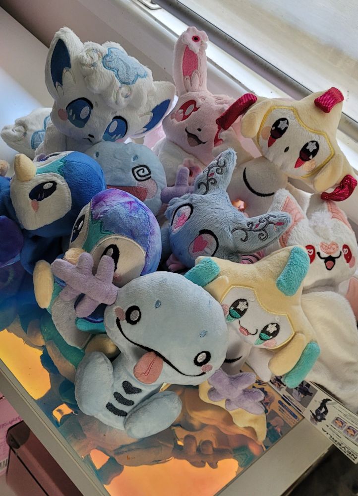 A small pile of 10 handmade plushies. It consists of mostly pastel coloured pokemon. 