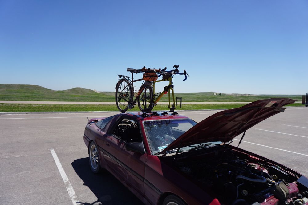 Two bicycles on roof rack attached to 80s Toyota Supra with the hood popped