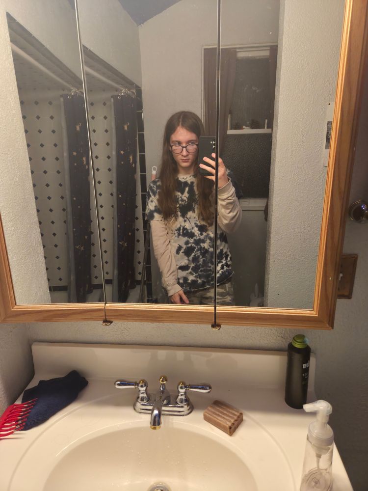 Me standing in a bathroom mirror with my phone up to take a photo. I'm wearing a blue and white tie-dye T-shirt over a white longsleeve.