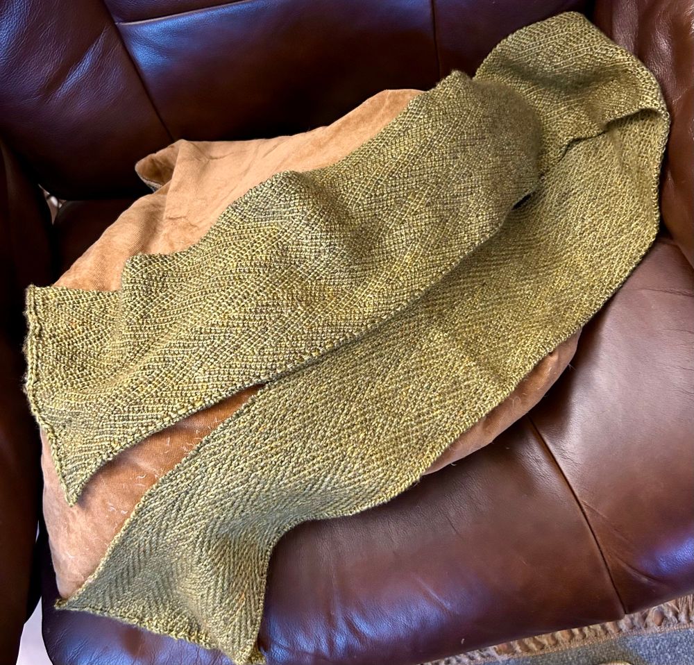 A narrow green hand knit scarf draped on a brown leather chair
