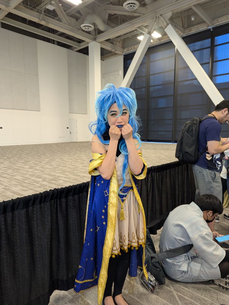 An Idia (from Twisted Wonderland/Twst) cosplayer in his Starsending robes with their hands up by their mouth timidly and looking ICly distressed