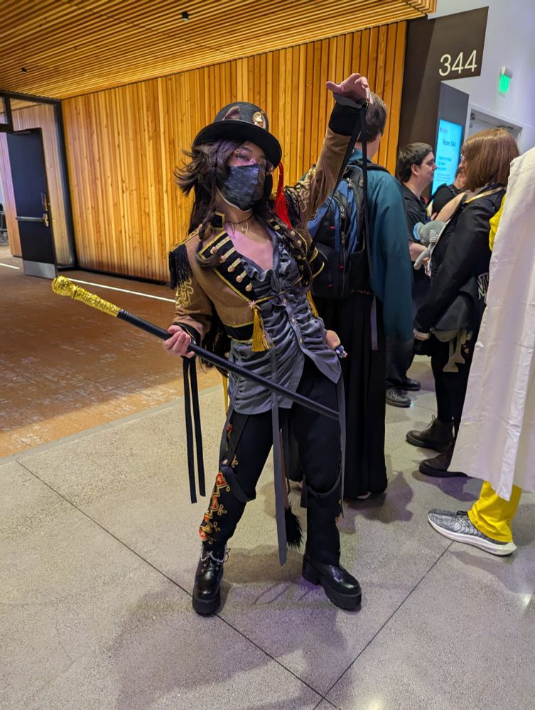 A Leona (from Twst) cosplayer with one hand held up as if being pulled by puppet strings and the other holding a cane, in his Playful Land attire. 