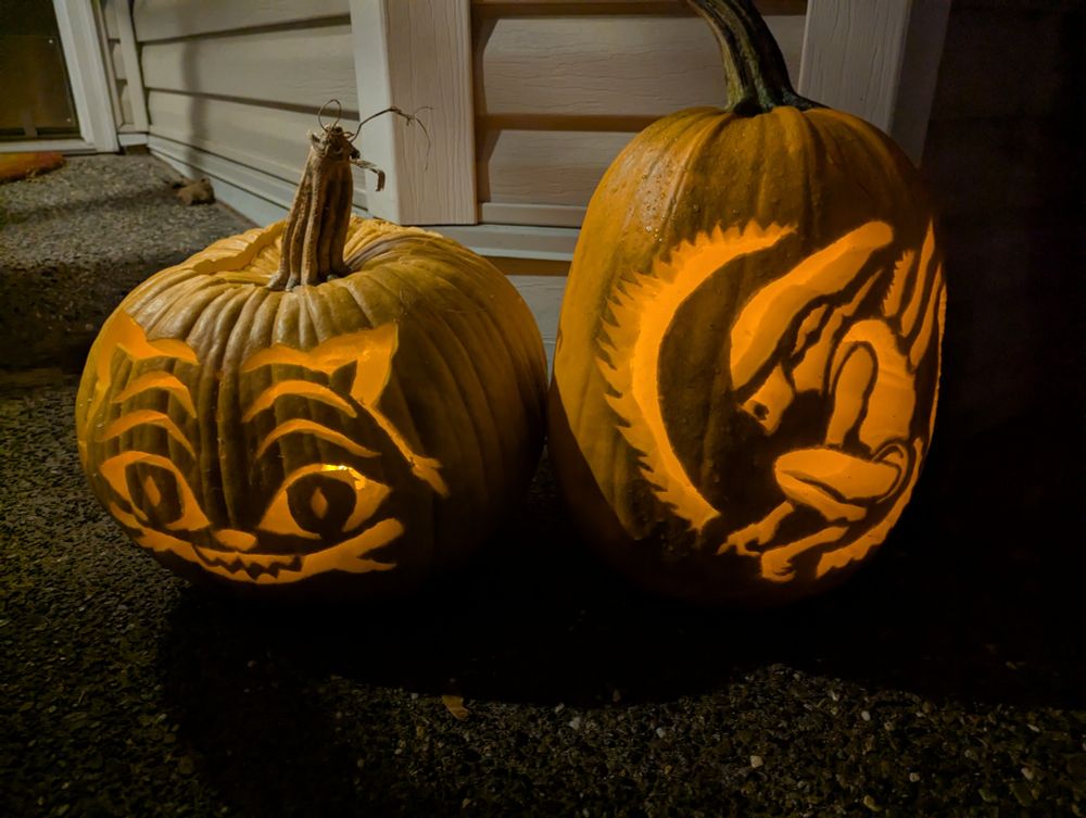 Two carved pumpkins in the evening, lit up. The stouter one on the left is carved as Derpy from Kpop Demon Hunters, the taller one on the right is a coiled Xenomorph in honor of Alien Earth this year