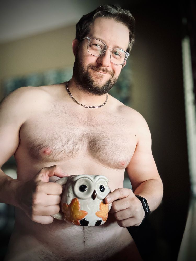 Gay boy standing by a window, basking in the perfect lighting as he sips his Sunday morning coffee from a fall owl ceramic mug.