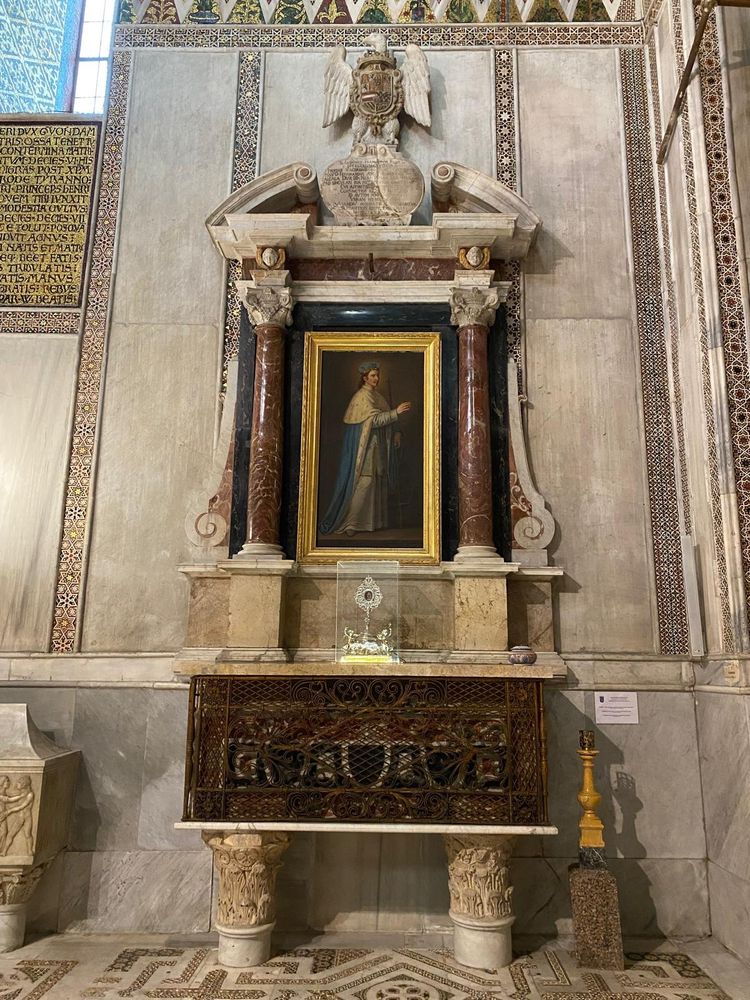 Tombeau de saint Louis à la cathédrale de Monreale en Sicile : sur un sol pavé, deux colonnes sculptées supportent un cercueil enserré dans une cage grillagée. Au dessus, le retable avec un tableau figurant saint Louis debout, encadré de deux colonnes de porphyre. Au fronton, une inscription en latin.