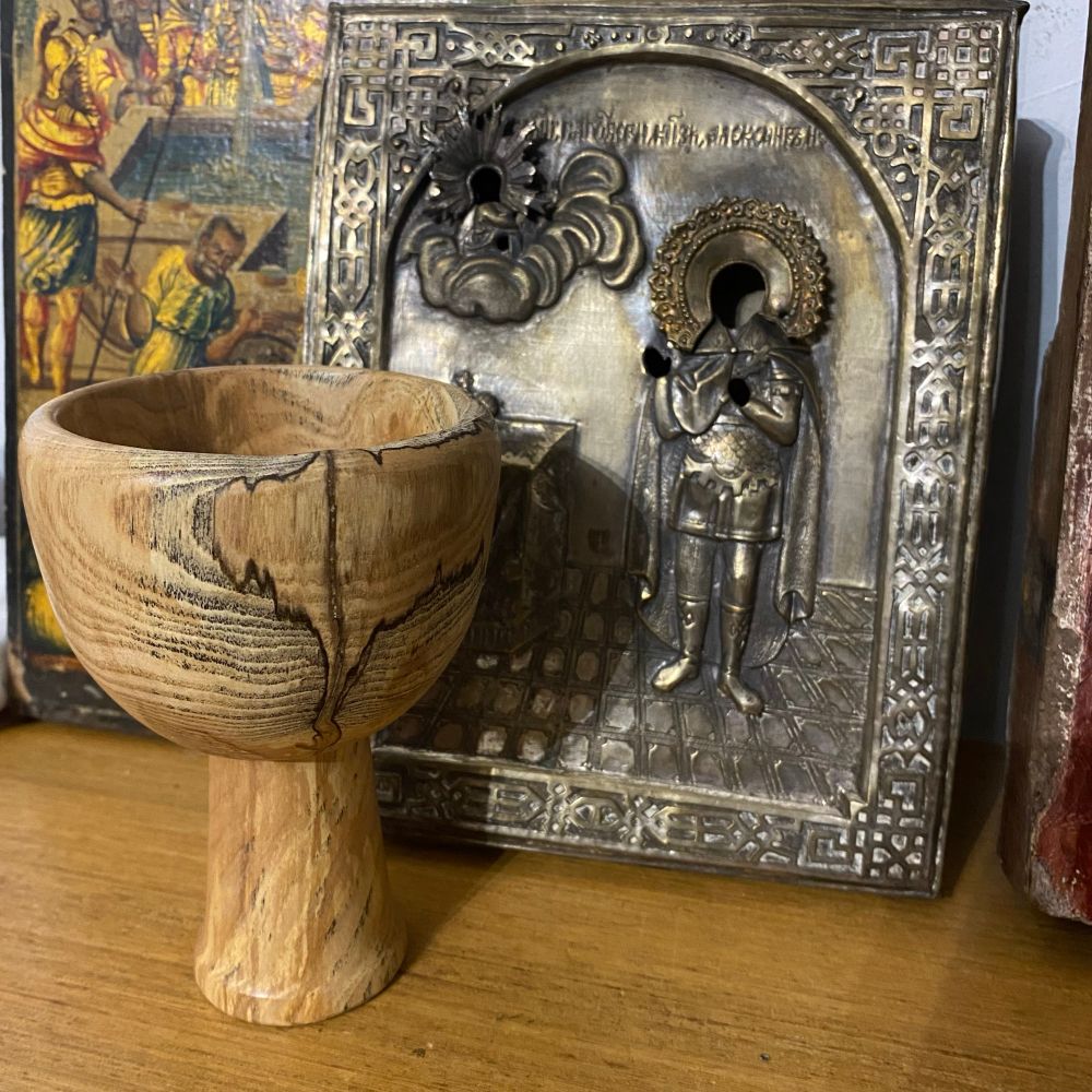 « saint Graal » en forme de calice en bois, avec des motifs formés par les nervures, posé sur un bureau en bois, avec des icônes en arrière plan