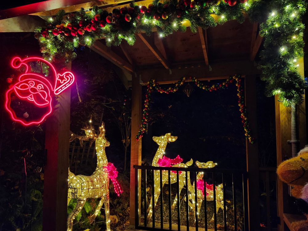 An entry way to a covered walkway with a red neon Santa face, lit garland with baubles, and a family of lit deer with red bows