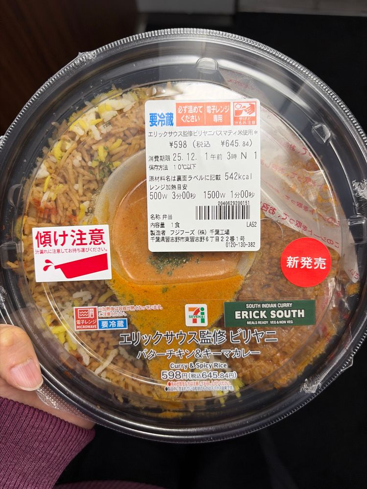 セブンイレブンの「エリックサウス監修ビリヤニ（バターチキン＆キーマカレー）」のパック商品を手に持っている様子。
