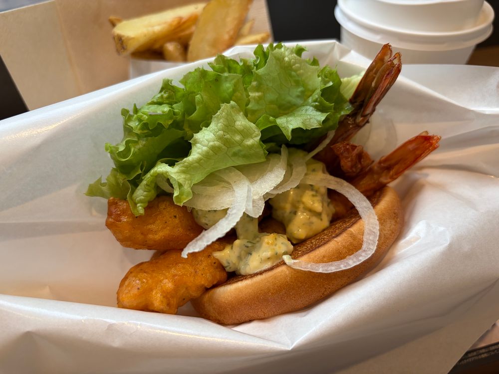 エビフライとレタス、オニオン、タルタルソースを挟んだバーガーの写真。奥にポテトとドリンクが見える。