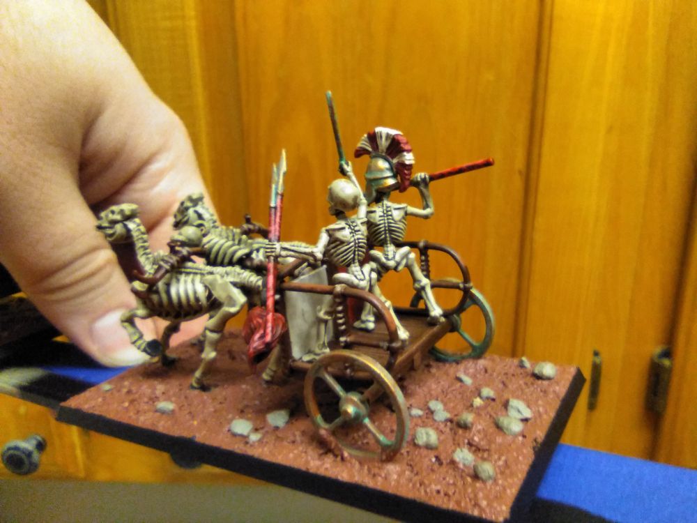 Miniature: Skeleton chariot #2, behind and to the side. Forward skull with curved ram horns. Bronze wheels corroded by verdigris.