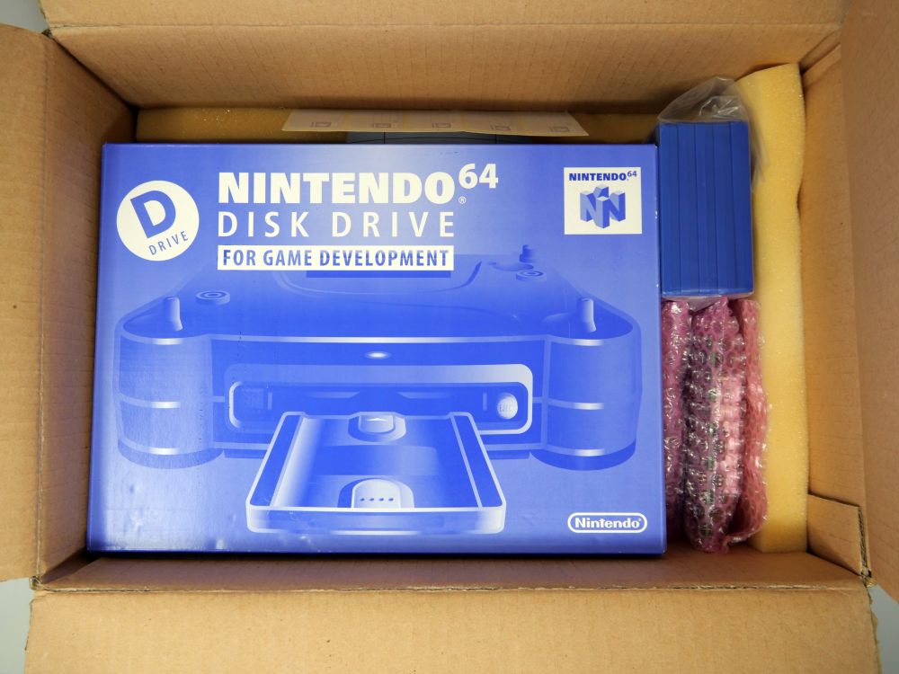 A picture of a carboard box with a smaller boxed Nintendo 64 Disk Drive (64DD) Development Kit inside of it. Yellow foam padding and some bubble wrap surround it.