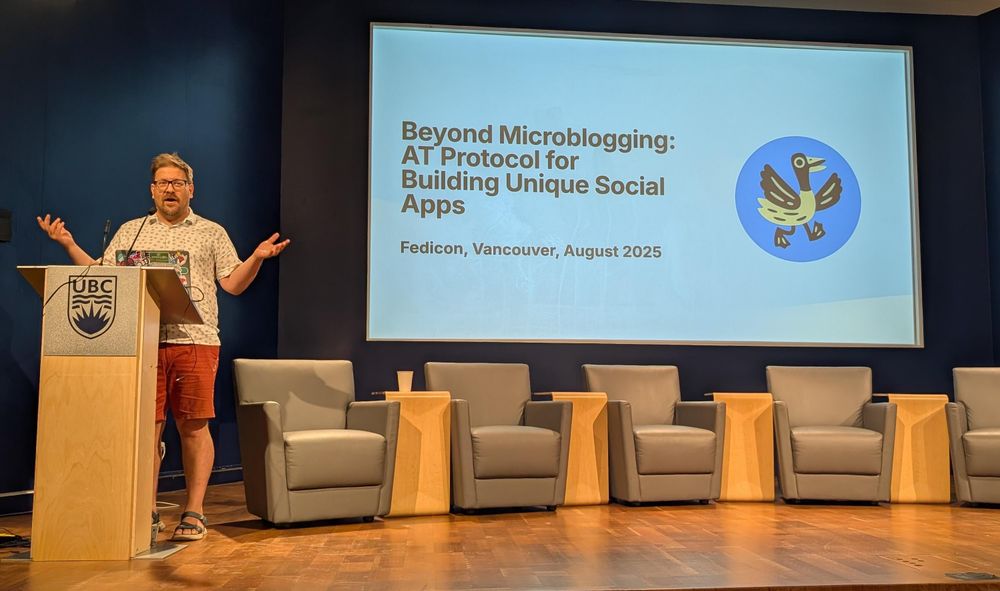 Boris stands on stage behind a podium in front of slide presentation 'beyond microblogging AT protocol for building unique socialmapps"