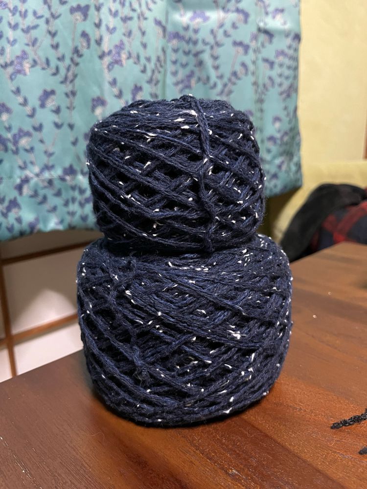 Photo of two tire-shaped balls of midnight-blue cotton yarn with white flecks throughout the strands, sitting stacked on a wooden table.