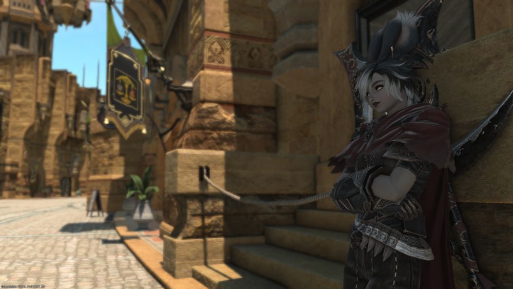 My WoL, a greyish-brown-skinned viera woman with black and grey hair leaning against a building in Ul Dah. She is wearing a red cloak and has a large, ornate scythe on her back. She's smiling as she looks down the street.