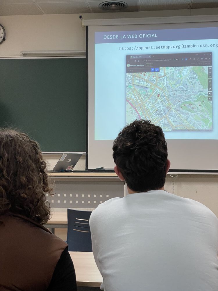 Gente de espaldas atendiendo . Se ve un mapa en la transparencia 
