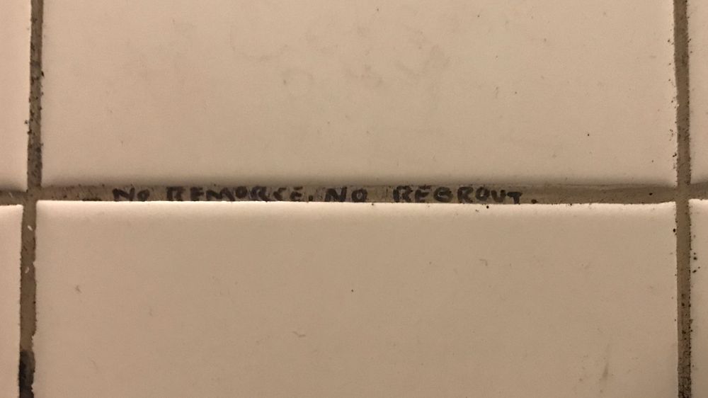 Black text written with a marker in a horizontal strip of grout at The Rose & Thistle Public House bathroom. It reads “No remorse, no regrout”. Found on April 27th, 2019