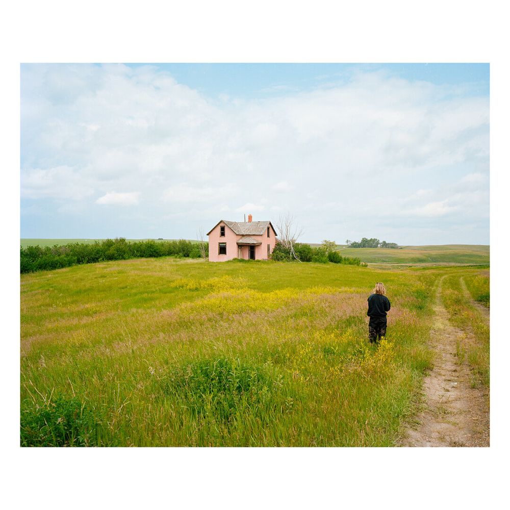A woman standing in front of a barn in Sescatuan. Image on film.