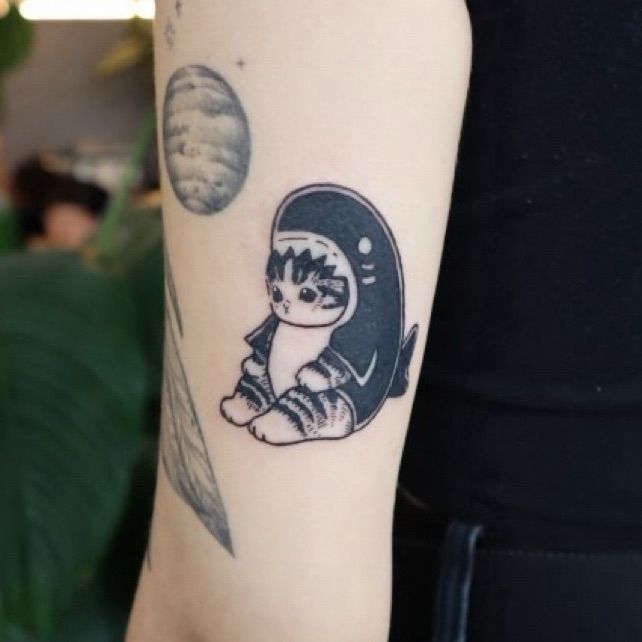 A photo of the back of my upper arm, with a fresh tattoo of mofusand's samenyan (a small cartoon cat wearing a shark costume)