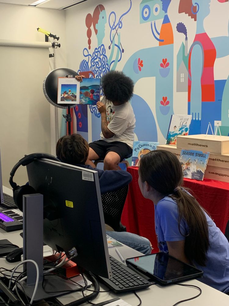 Mychal reads a book aloud to teens at the New York Public Library; the teens lean forward and listen!