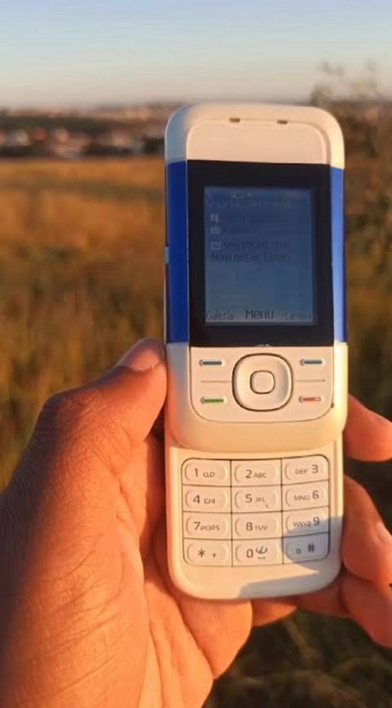 Nokia 5200. Tirei a imagem da internet, está ensolarado e uma pessoa de pele negra segura o celular aberto, que está em primeiro plano. Ao fundo, um campo verde. O celular é daqueles que vc puxa para cima e revela o teclado.