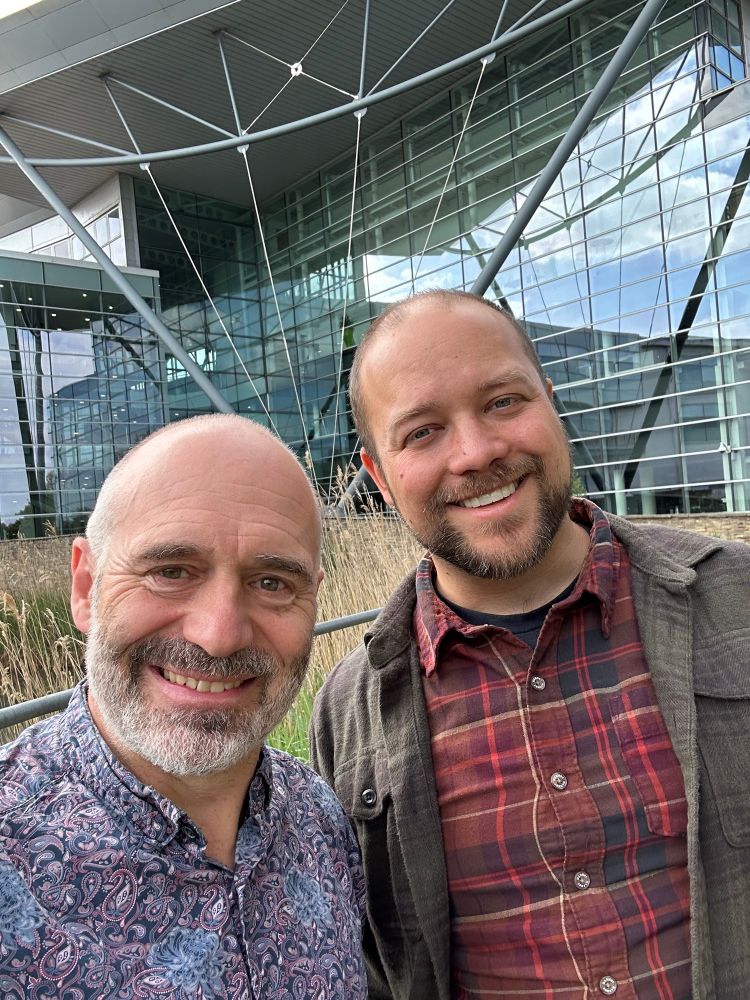 Photo of 2 climate scientists, Richard Betts and Zeke Hausfather, in front of the glass-fronted building of the Met Office HQ