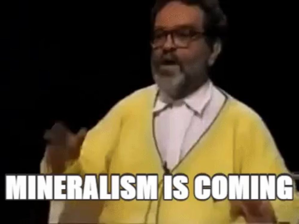 a man with a beard and glasses is wearing a yellow sweater and a white shirt and says mineralism is coming .