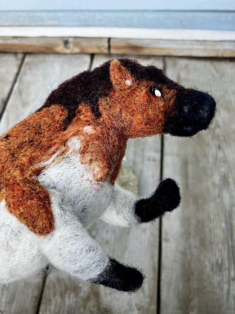 A close up photo of a needlefelted horse in the style of a Lascaux cave painting.