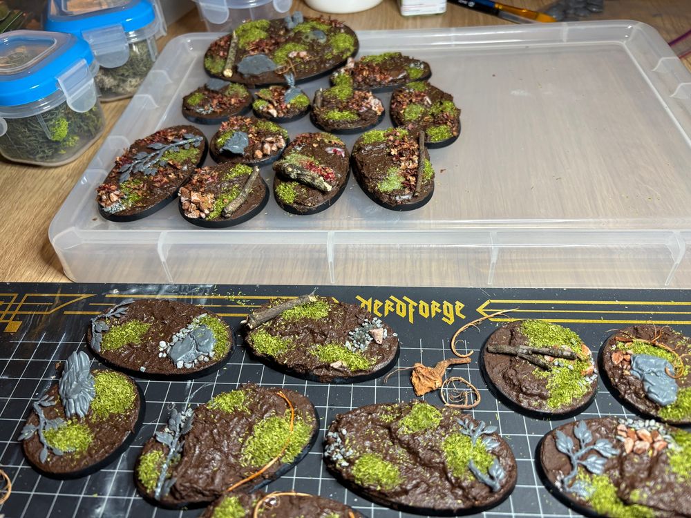 A selection of Age of Sigmar miniature bases, partway through being built up as a forest setting