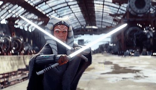 a woman in a star wars costume holds two lightsabers in front of a building