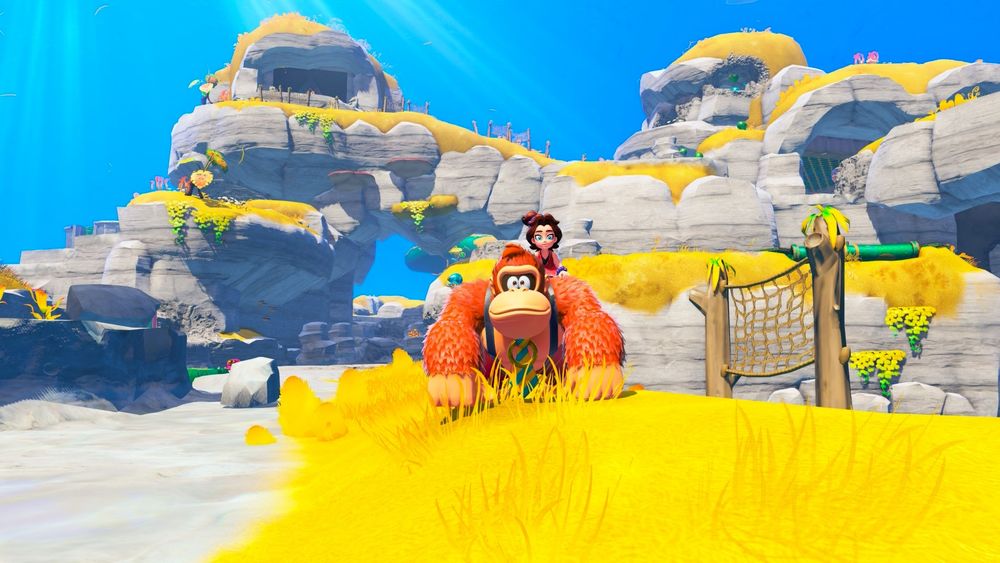 Donkey Kong and Pauline faces the camera. They stand on yellow grass with mountainous cliffs of grey and a brilliant blue sky behind them. Cliffs have partially been destroyed, now featuring holes and damage across them.