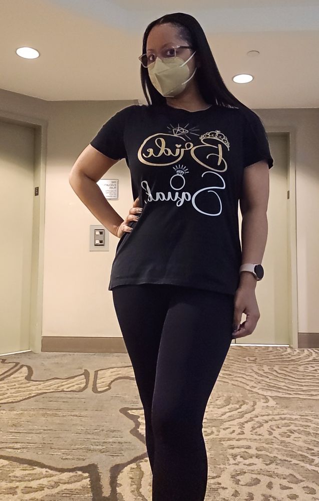 author in black outfit with gold accented "bridal party" lettering, matching gold-tan mask