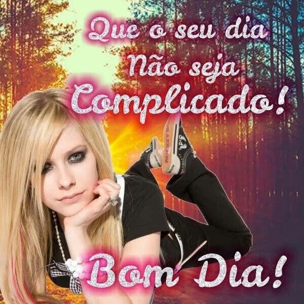 Montagem com a Avril Lavigne (mulher jovem loira de cabelos lisos) deitada de bruços, com os pes pra cima e com a mão no queixo e cara meio séria, com uma floresta ao fundo. Com mensagem "que seu dia não seja complicado! Bom dia!" escrita em fonte jovial com glitter e sombra rosa.
