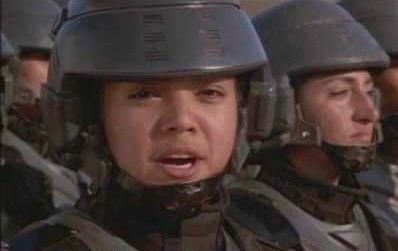 A frame from propaganda commercial in the movie Starship Troopers. Soldiers in uniform are standing in a line, and the one closest to us is looking at the camera while she is mid-sentence. The image is usually captioned with the line "I'm doing my part!"