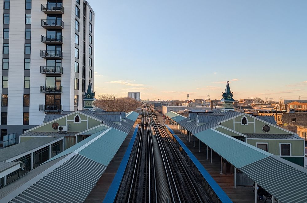 photo taken of the Ashland Pink/Green CTA stop from above the tracks in a pedestrian overpass showing the train tracks going off into the distance and an (barely visible) approaching train